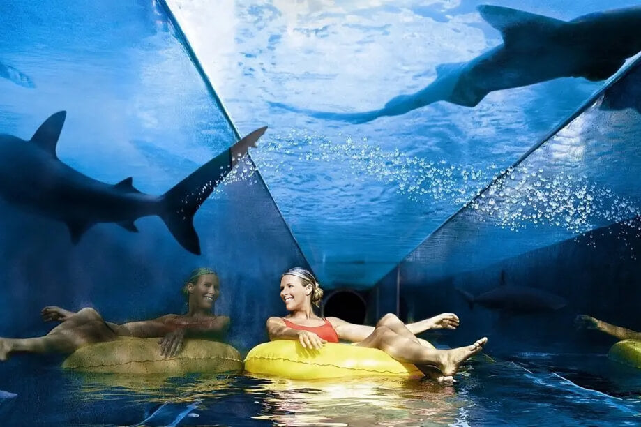 Woman floating on a tube through a transparent tunnel slide with sharks swimming overhead at Atlantis Aquaventure Waterpark, Dubai.