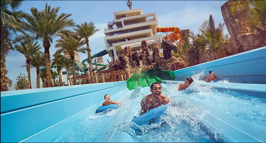 Thrill-seekers racing down water slides at Atlantis Aquaventure Waterpark in Dubai, surrounded by palm trees and iconic attractions.