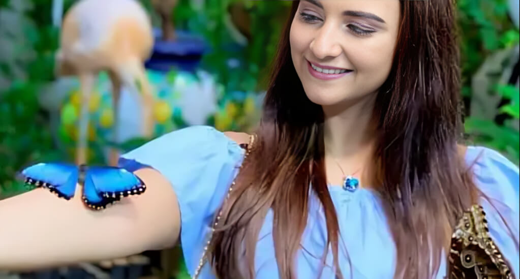 Smiling woman interacting with vibrant butterflies at the Butterfly Garden Dubai, surrounded by lush greenery.
