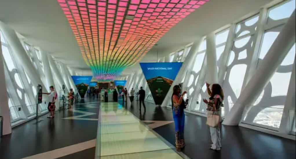 Visitors exploring the top walkway of Dubai Frame, featuring panoramic views, a glass floor, and colorful LED ceiling lights.