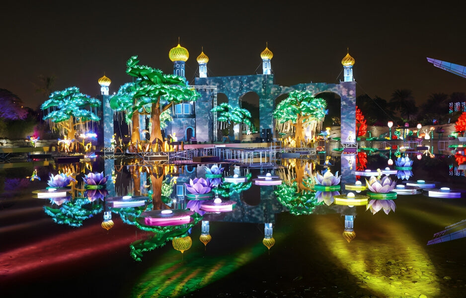 Enchanting illuminated palace, glowing trees, and floating lotus lights reflected on water at Dubai Garden Glow during nighttime.