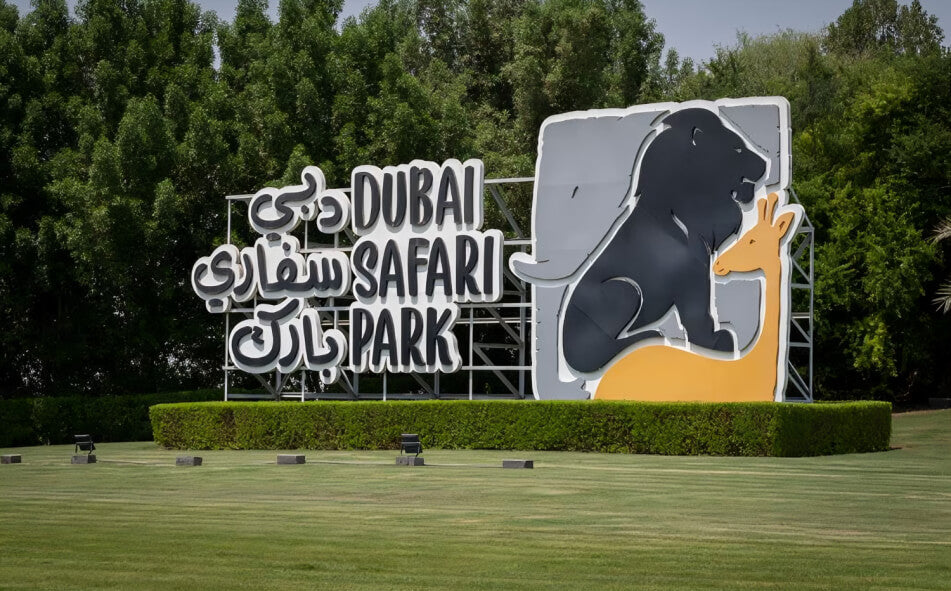 Entrance sign of Dubai Safari Park featuring lion and giraffe artwork, set against lush greenery.