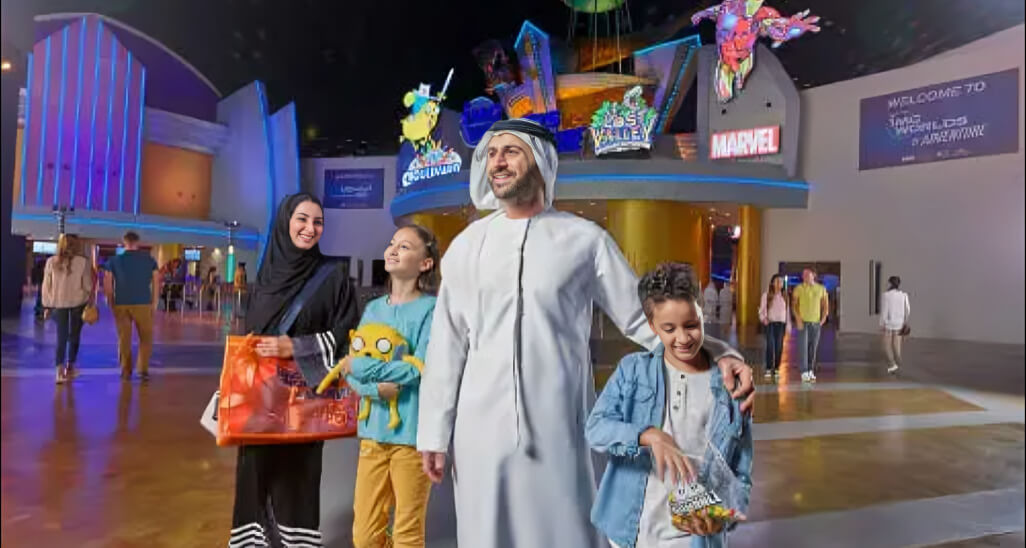 Happy family enjoying their visit at IMG worlds of adventure Dubai, with themed zones like Marvel, Cartoon Network, and Lost Valley in the background.
