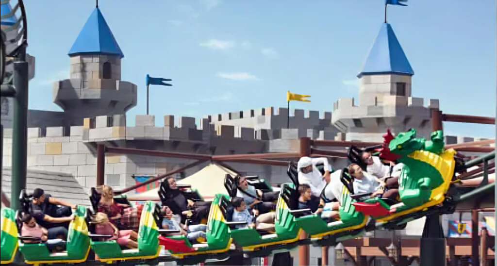 Families enjoying a dragon-themed roller coaster ride in the medieval castle zone at LEGOLAND Dubai Park.