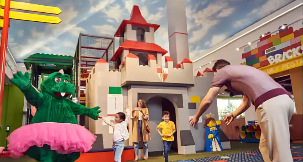 Children playing and meeting a friendly dragon mascot inside the indoor LEGO castle play area at LEGOLAND Dubai theme park.