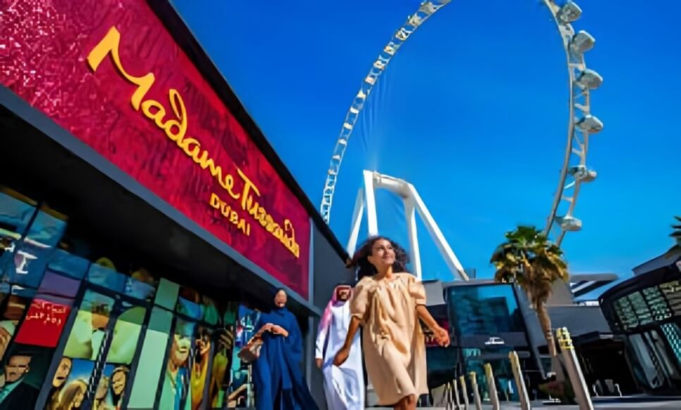 Exterior view of Madame Tussauds Dubai with visitors walking by, featuring the iconic Ain Dubai Ferris wheel in the background on a clear sunny day.