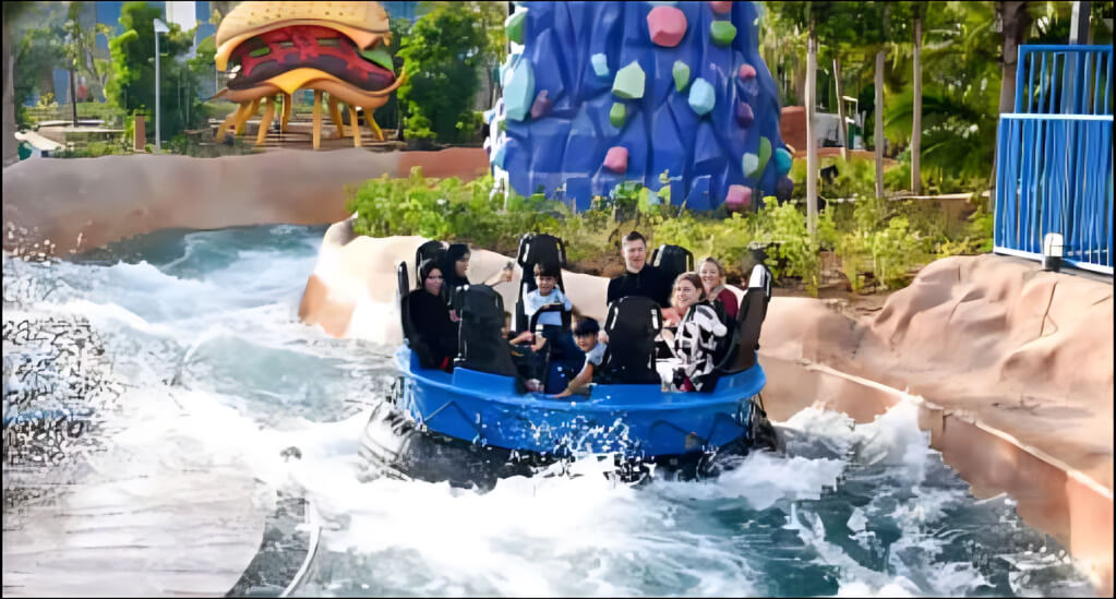 Family enjoying a thrilling water raft ride at Motiongate Dubai theme park, surrounded by colorful cartoon-themed structures and lush greenery.