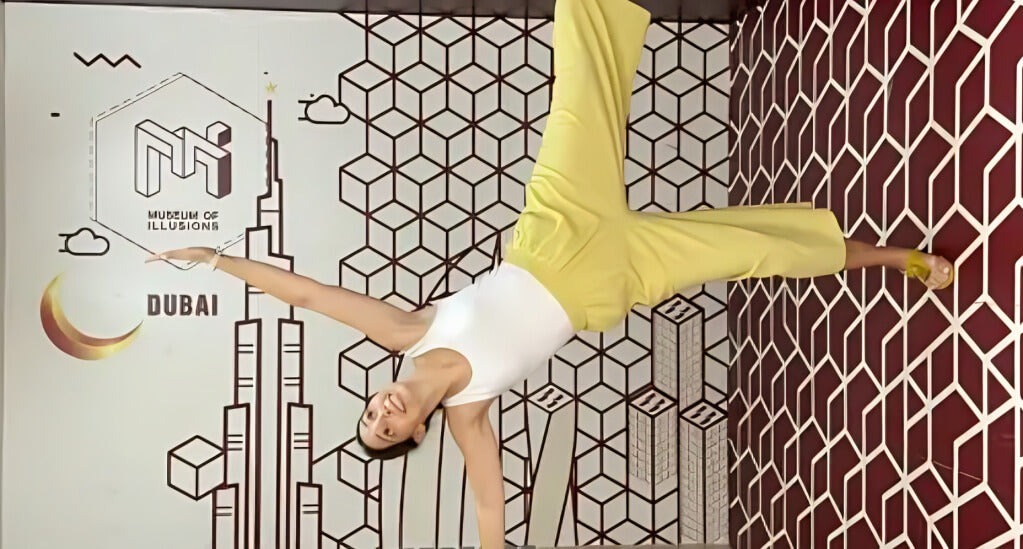 Visitor defying gravity in a tilted room illusion at the Museum of Illusions Dubai, surrounded by geometric patterns and surreal visual effects.
